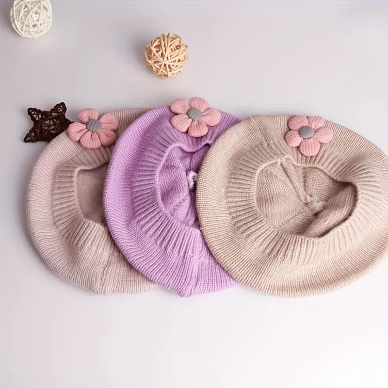Trois bérets fille en maille rose pâle, lilas et beige, vus de l’intérieur avec fleurs décoratives.